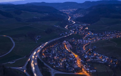 Aerial night view of a smart city with illuminated highways and neighborhood lights, illustrating “Connected Life” digital infrastructure, mobility, and IoT networks.