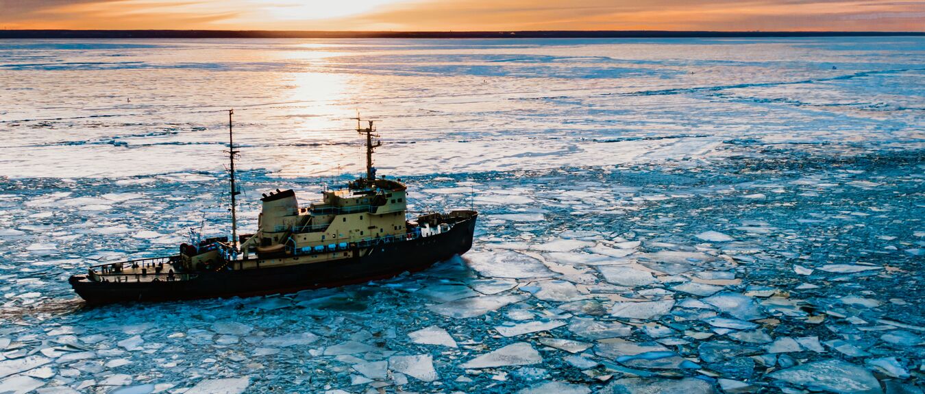 Ships sail through cold sea water covered with broken ice pieces to bay terminal under blue cloudless sky aerial pull